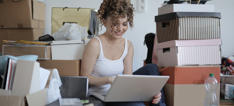 A woman sitting next to boxes and using a laptop